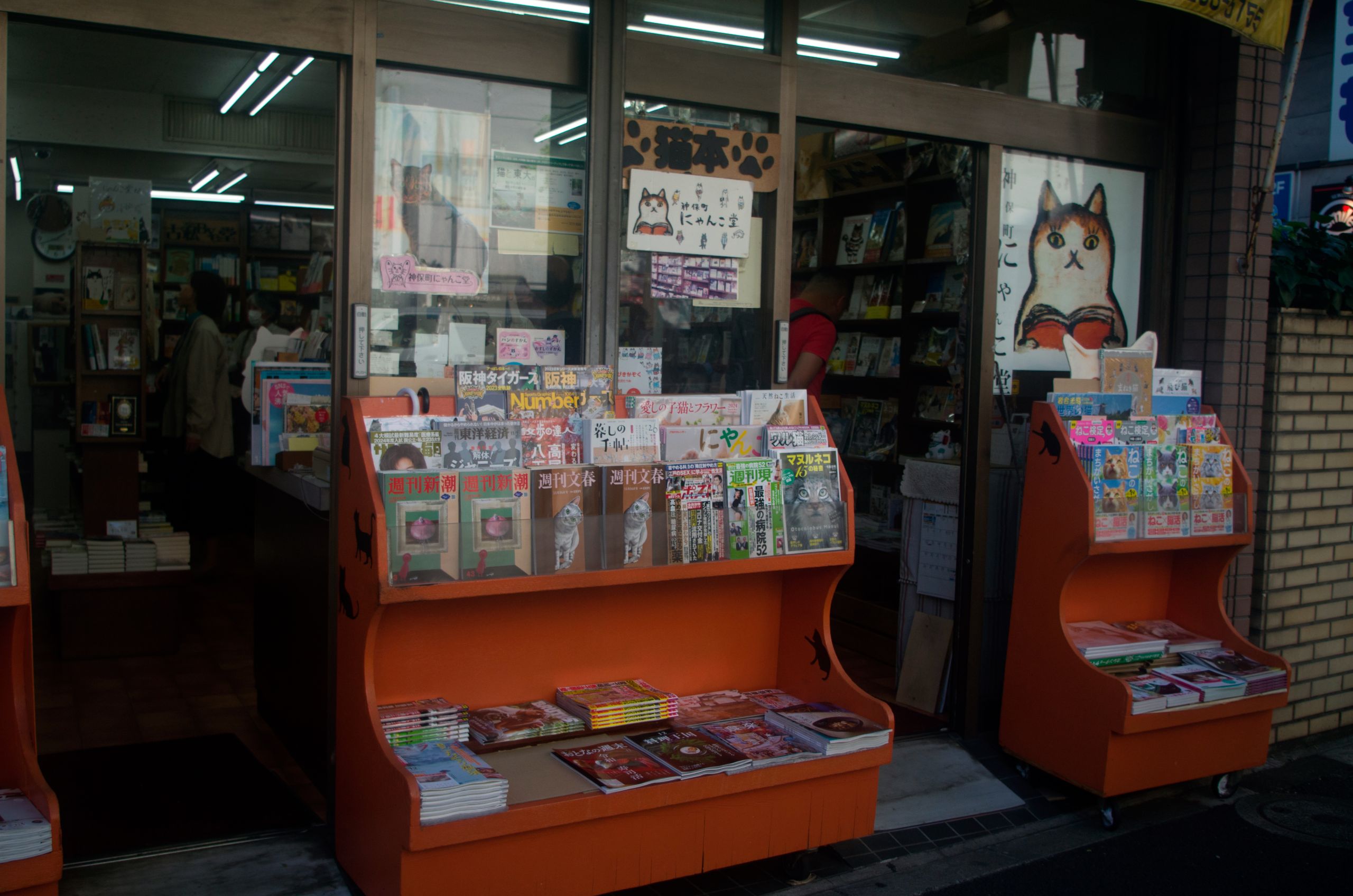 Eingang einer auf Katzenliteratur spezialisierten Buchhandlung in Jimbochō, Tokyo, mit orangefarbenen Regalen voller Bücher.